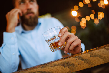 A young handsome caucasian  businessman with a beard is sitting in a cafe drinking whiskey and talking on the phone. Work in a restaurant