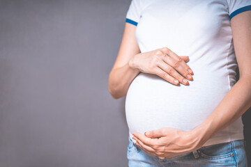 Pregnant woman holds hands on belly on a gray background. Copy space, pregnancy, motherhood, people and expectation concept. Close-up, copy space, indoors. Toned photo of pregnancy.