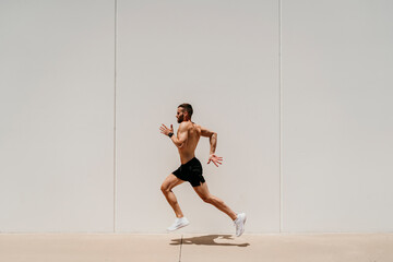 Barechested male athlete running along a wall