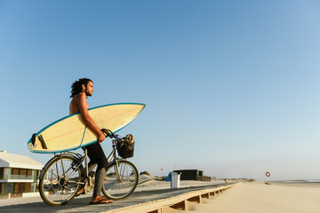 Surfer riding a bicycle during the sunset, holding surf board