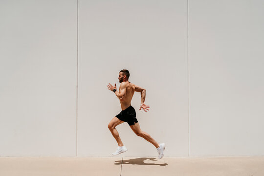 Barechested male athlete running along a wall