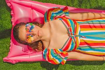 Portrait of woman wearing glasses with colorful pom poms relaxing on pink airbed