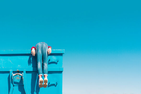Young man hanging over edge of blue container, rear view