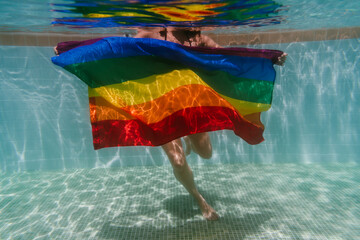 young woman in a pool holding rainbow gay flag underwater.LGBTQ concept. Summertime