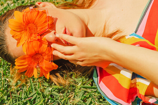 Portrait of woman lying on a meadow wearing glasses with orange flowers covering her eyes