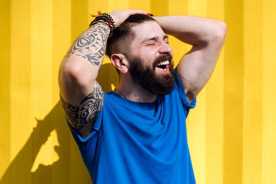 Laughing young man with tattoo standing in front of yellow wall