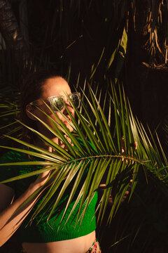 Woman with sunglasses hiding behing palm leaves
