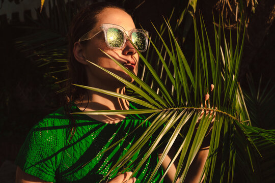 Woman with sunglasses hiding behing palm leaves
