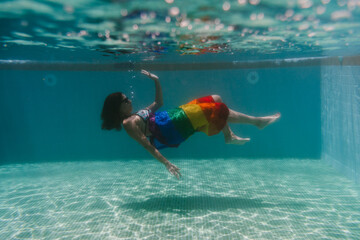 young woman in a pool holding rainbow gay flag underwater.LGBTQ concept. Summertime