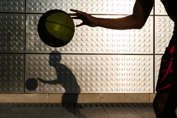 Young man playing basketball at a metallic shining wall