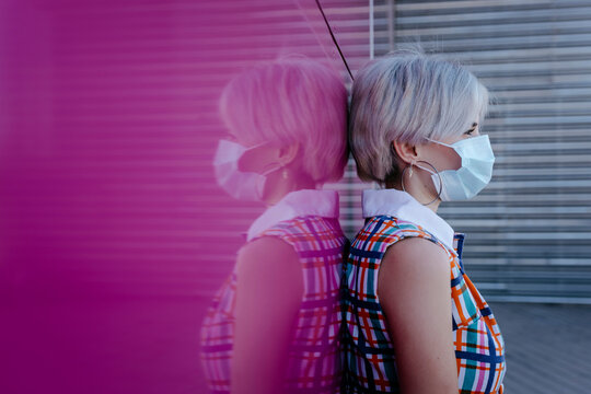 Young woman wearing mask standing against pink glass wall