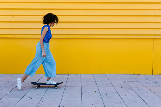 Young woman skateboarding in front of yellow wall