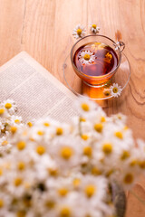 A cup of hot herbal tea with chamomile flowers opened book on a wooden table. Morning breakfast background.