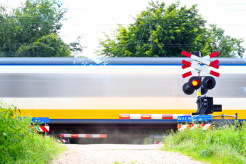 Dutch train passes a railway crossing in a natural agricultural area. This railway crossing is secured with boom barriers and warning lights.