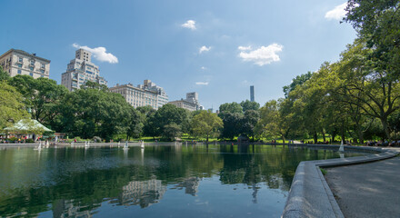 Panoramic image of central park model boat sailing during summer with mirror effect on water...