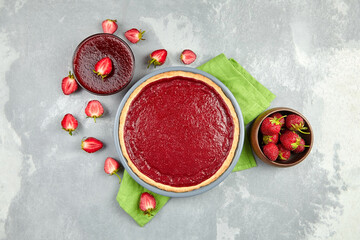 Strawberry pie in backing dish with jam and fresh berries on grey concrete background