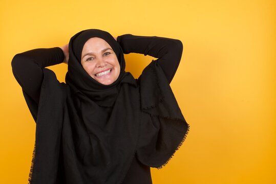 Beautiful Middle Aged Muslim Woman Wearing Black Hijab Over Yellow Background Stretching Arms, Relaxed Position.