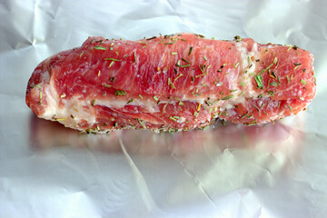 A piece of bright red pork neck seasoned with dried herbs and salt on a brightly reflective foil