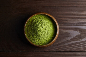Freeze dried wheatgrass powder in wooden bowl on dark background. Top view.