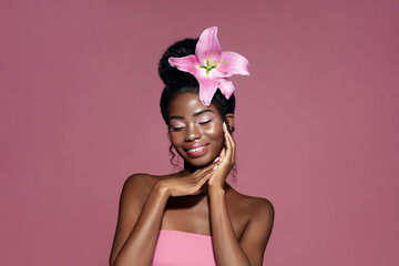 Tenderness. Young Beauty African American model with pink lily flower in the hair touching face