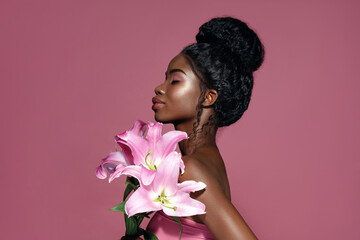 Profile portrait of young beautiful African American model posing with lily flowers against pink background