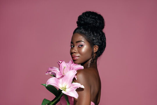 Beauty and Spa. Attractive African American young model holding  lily bouquet and posing against pink background