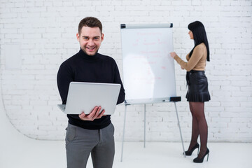 Manager businessman male announcer stands with a laptop while a woman writes a business promotion...