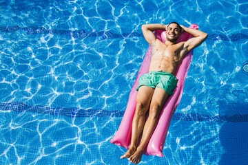 Shirtless handsome young man with hands behind head relaxing on airbed in swimming pool