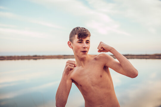 Portrait of smiling teenage boy showing boxing gesture by lake