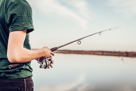 Midsection of teenage boy fishing with rod in lake while standing against cloudy sky