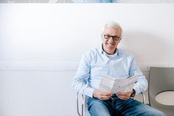 Senior man sitting in waiting room of medical practice, reading leaflet