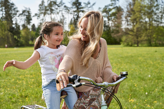 Smiling blond woman looking at daughter enjoying bicycle ride with arms outstretched