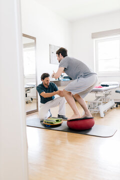 Physiotherapist assisting patient, practicing on balance trainer
