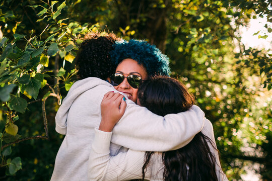 Loving children embracing mother with blue hair against trees in park