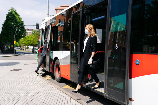Mature businesswoman wearing protective mask getting off public bus, Spain