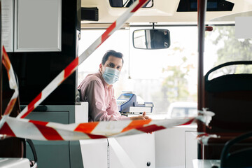 Portrait of mature bus driver wearing protective mask behind caution tape in public bus, Spain