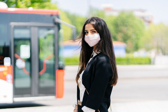 Portrait of young woman wearing protective mask waiting at bus stop, Spain