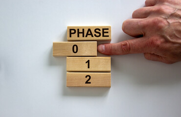 Wooden blocks form the words 'phase, 0, 1, 2,' on white background. Male hand. Business concept. Copy space.