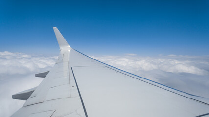 Airplane wing above clouds and blue sky. The concept of flight, travel, air transportation.