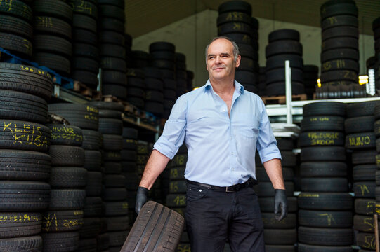Confident senior male owner holding tire while working at store