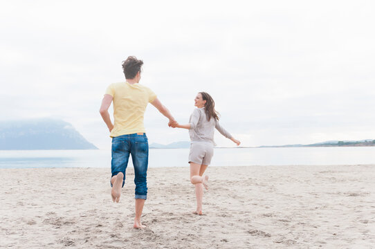 Happy couple running hand in hand on the beach, Sardinia, Italy