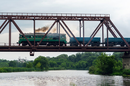 Freight train rides on a railway bridge over the river