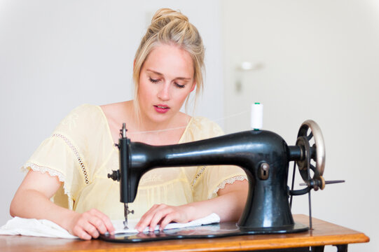 Portrait of blond young woman using old sewing machine