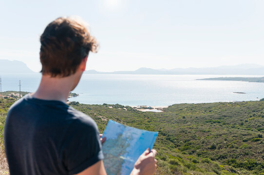 Back view of man with map looking at view, Sardinia, Italy