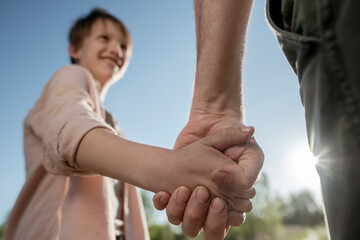 Father holding daughter hands while standing against clear sky in park during sunny day