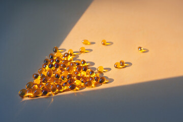 Gelatin capsules in a ray of light on a yellow background. Dietary supplement, health care, soft focus.
