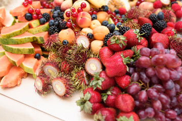 Abundance of many different fruits and berries on the table: grapes, strawberries, raspberries, currants, blueberries, blackberries, lychees, passion fruit, dragon fruite, longan, papaya.