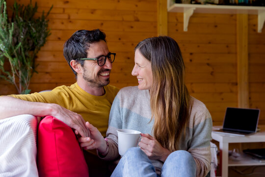 Romantic couple looking at each other while relaxing on sofa in log cabin