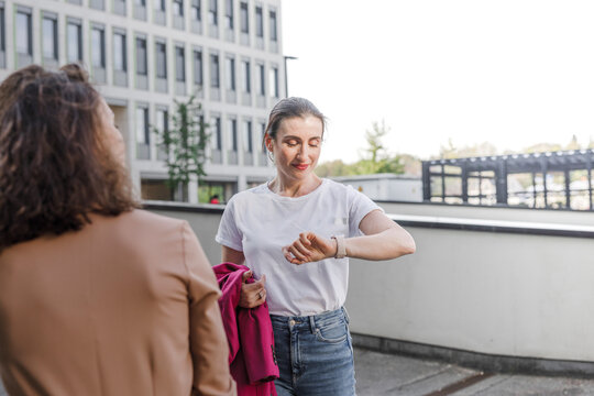 Businesswoman checking smart watch while standing with colleague outside office building