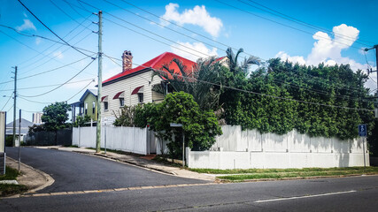 Street corner in Brisbane suburbs with red-roofed house surrounded by white picket fence an...
